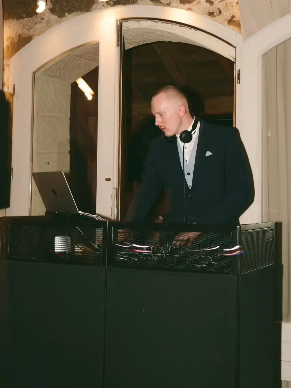 WMAX, Hochzeits-DJ, im Anzug am DJ-Pult vor einem Rundbogenfenster